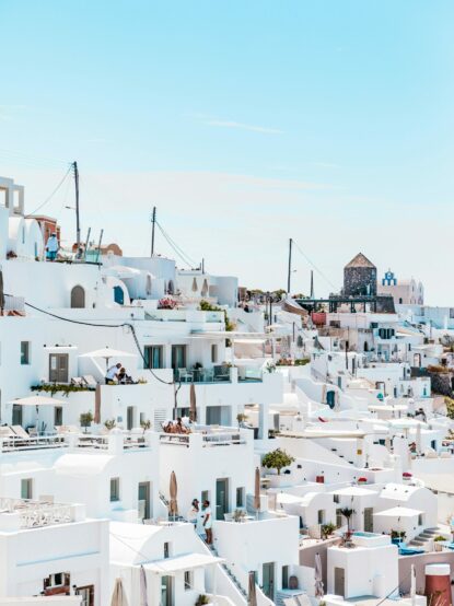 Pittoresco villaggio costiero con case bianche disposte su terrazze, tipiche delle località mediterranee. Balconi e terrazze offrono viste panoramiche sul mare e sul cielo limpido, evocando una sensazione di relax e tranquillità